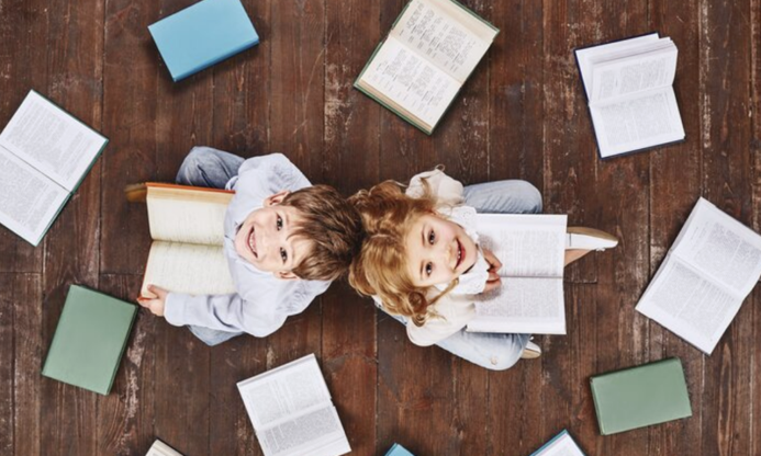 Una ni&ntilde;a y un ni&ntilde;o miran al techo rodeados de libro
