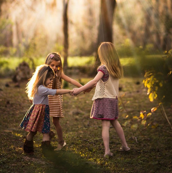 Tres ni&ntilde;as bailan en un bosque oto&ntilde;al d&aacute;ndose la mano