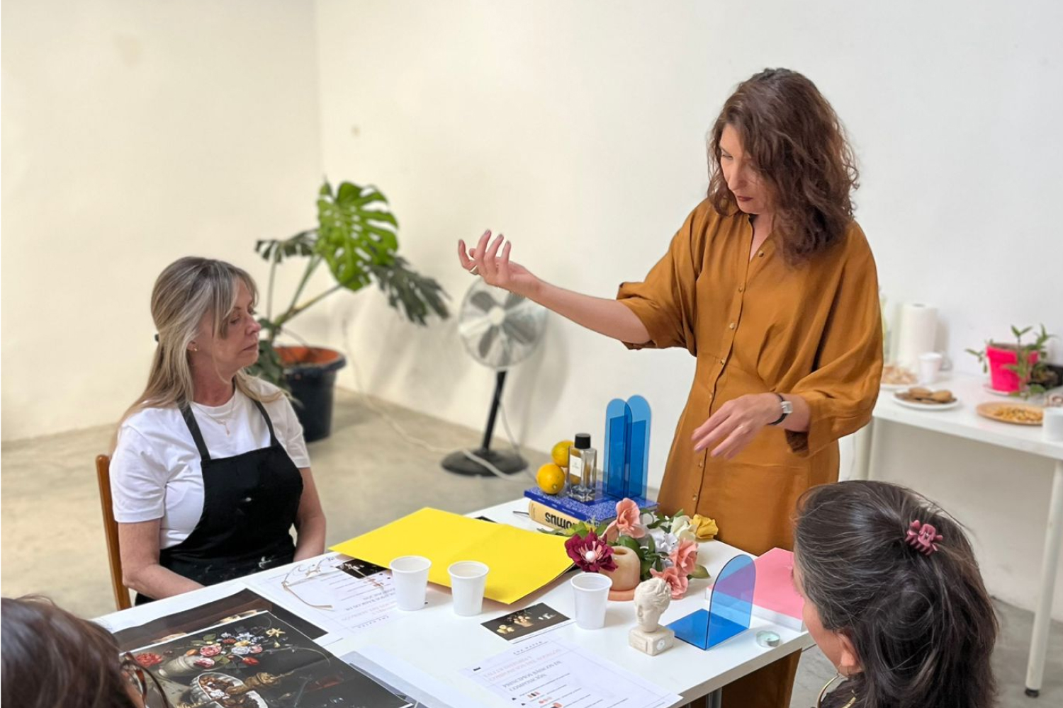 Mujer explica algo a otras dos mujeres con elementos sobre una mesa