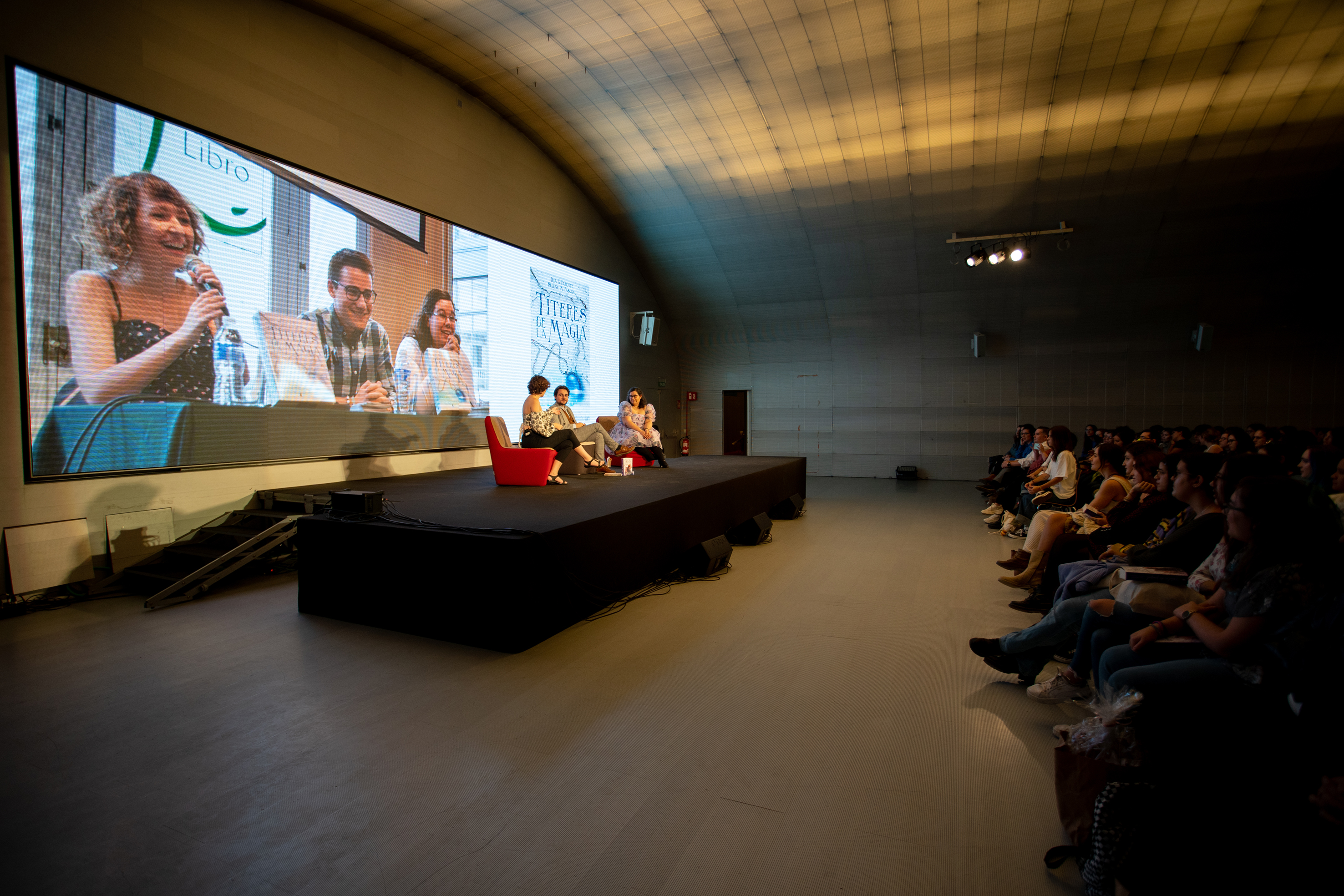 Conferencia en un auditorio con pantalla y tres ponentes