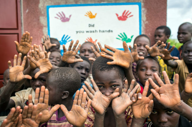 © UNICEF/UN03212/Ose Alumnos delante de un aviso que promueve el lavado de manos en una escuela primaria en el Distrito de Kiryandongo.