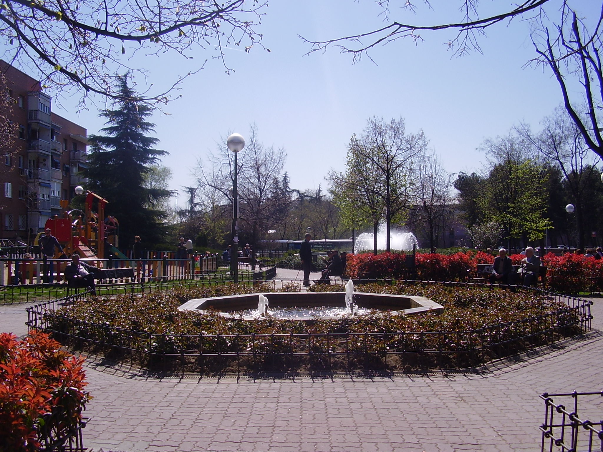 Se observa una fuente, diferentes arbustos y &aacute;rboles y una zona infantil